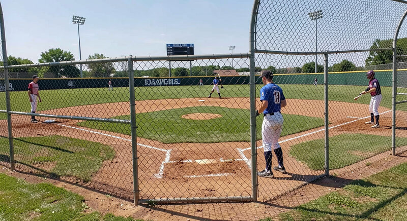A softball diamond seen from behind the backstop with fielders at their positions and a batter at the plate.